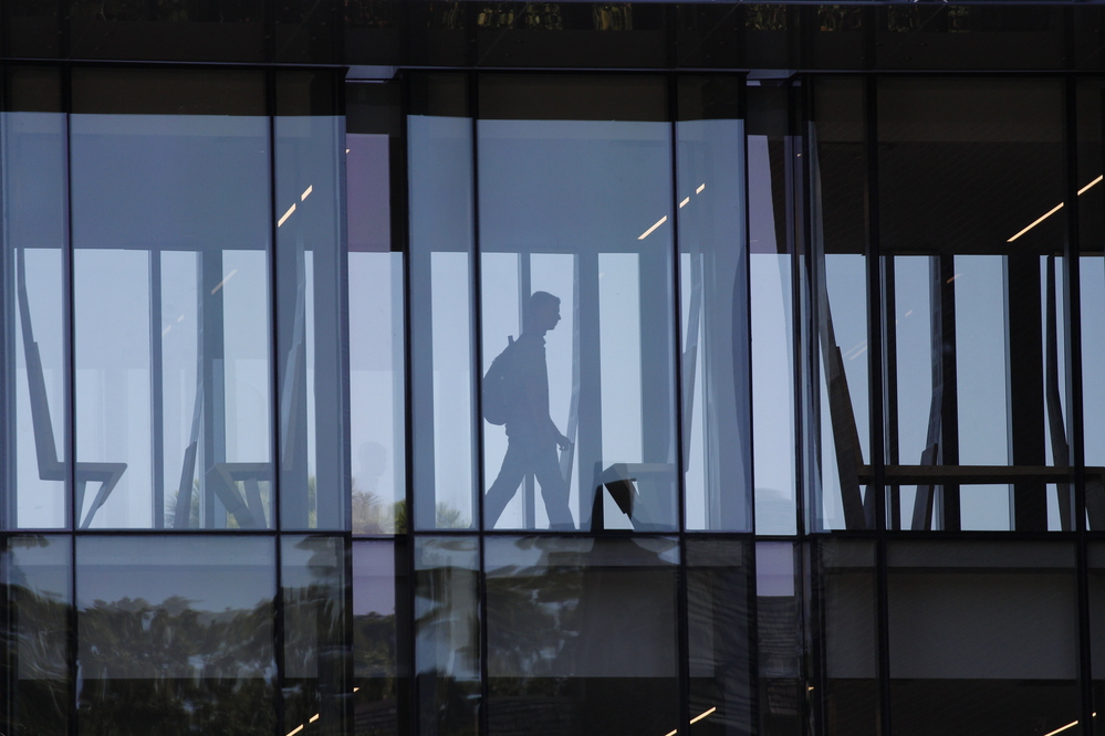 Silhouette of an individual walking through a glass-enclosed corridor inside a modern building.