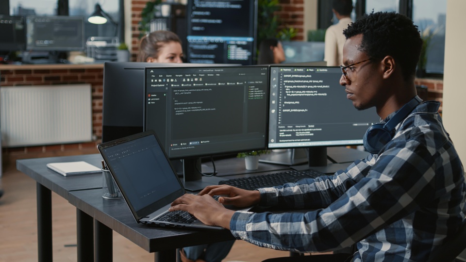 Person sitting at computer typing, surrounded by kiosks with other workers